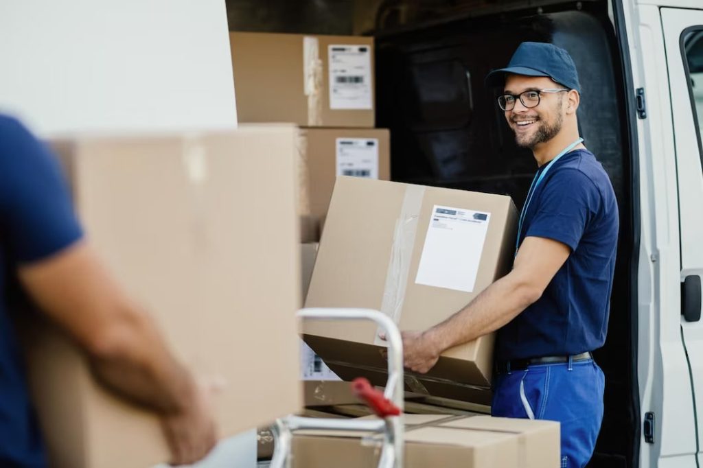 Happy manual worker carrying cardboard boxes to delivery van