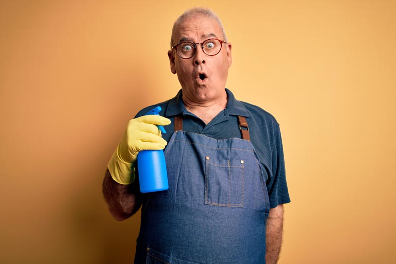 Middle age man wearing a cleaning apron and gloves with a cleaner