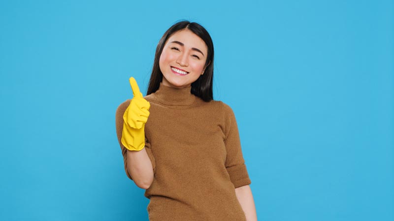 Smiling maid wearing yellow rubber gloves while doing a thumbs up gesture